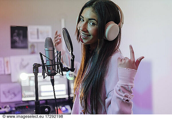 Smiling female singer wearing headphones gesturing while singing in studio