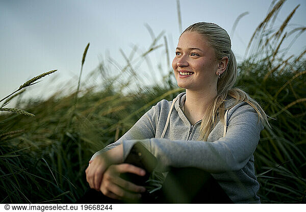 Smiling female sitting in countryside field and admiring nature