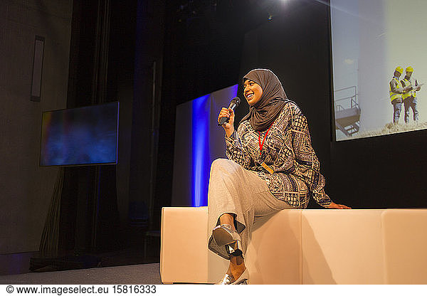 Smiling female speaker with microphone in hijab on stage