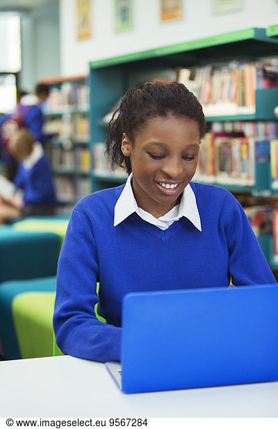 Smiling female student wearing blue school uniform using laptop in library