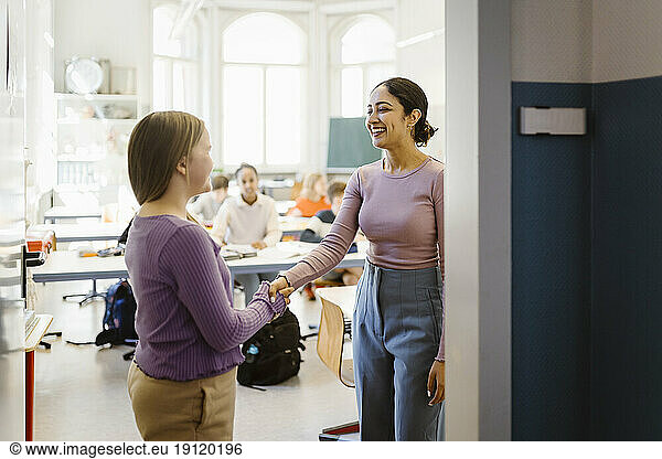 Smiling female teacher doing handshake with student standing in classroom