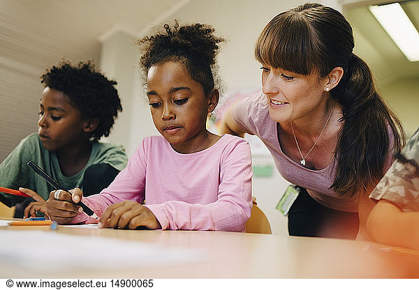 Smiling female teacher looking at students drawing in class