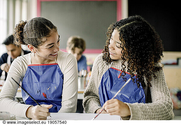 Smiling female teenage students talking during art class at high school
