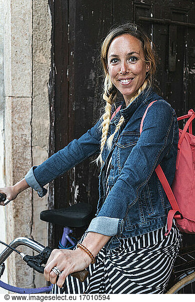 Smiling female tourist sitting on bicycle with backpack