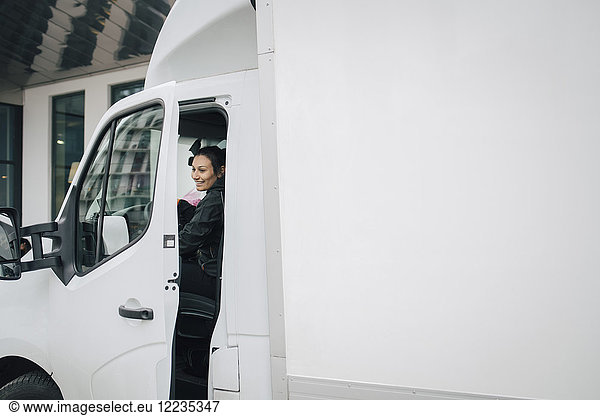 Smiling female worker closing door of white delivery van