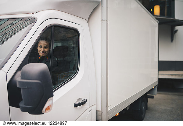 Smiling female worker driving white delivery van in city