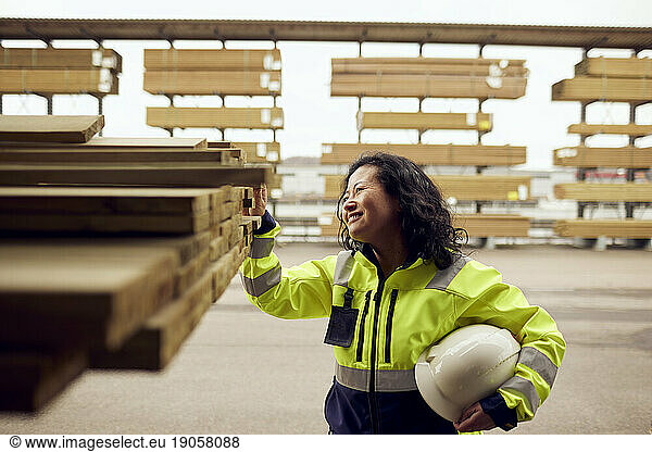Smiling female worker examining planks stacked at lumber industry