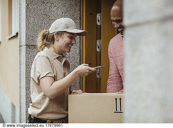 Smiling female worker taking photo of package while delivering to male customer