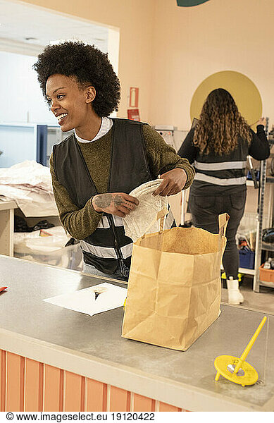 Smiling female worker with paper bag on counter at recycling center
