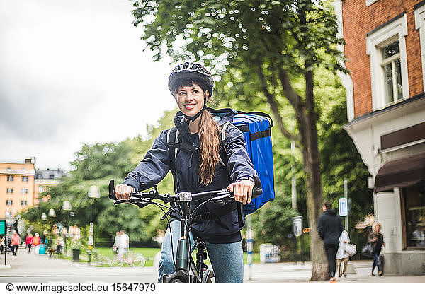 Smiling food delivery woman with bicycle on street in city