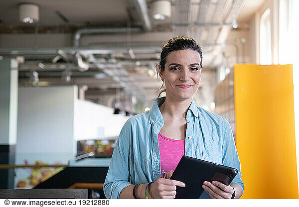 Smiling freelancer holding tablet PC standing in office cafeteria