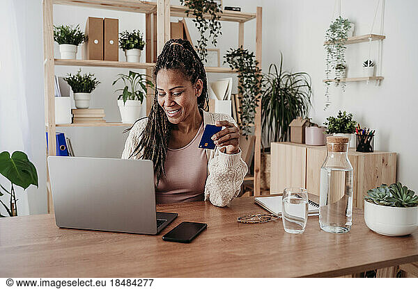 Smiling freelancer paying with credit card on laptop at home office