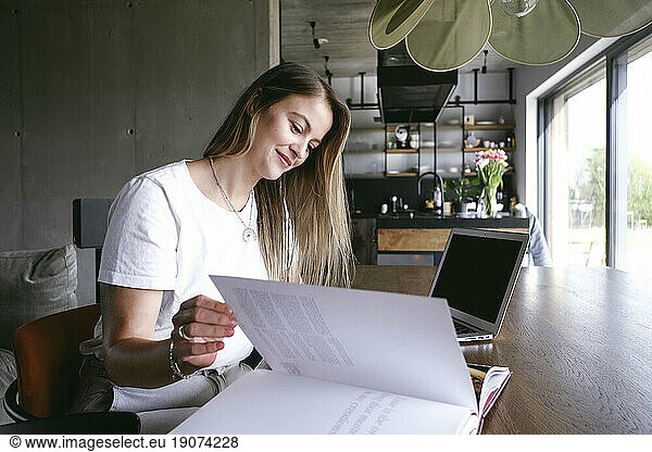 Smiling freelancer turning page of book at home