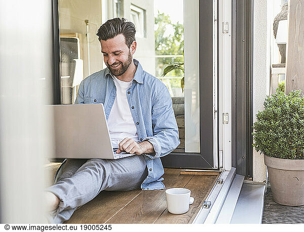 Smiling freelancer using laptop on floor in doorway at home