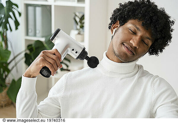 Smiling freelancer using massage gun at home office