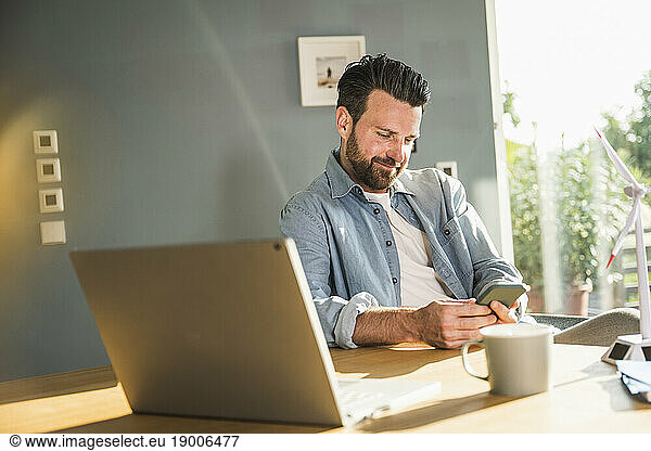 Smiling freelancer using smart phone at desk in home office