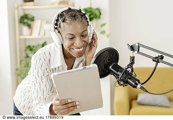 Smiling freelancer using tablet PC and recording podcast through microphone at home office