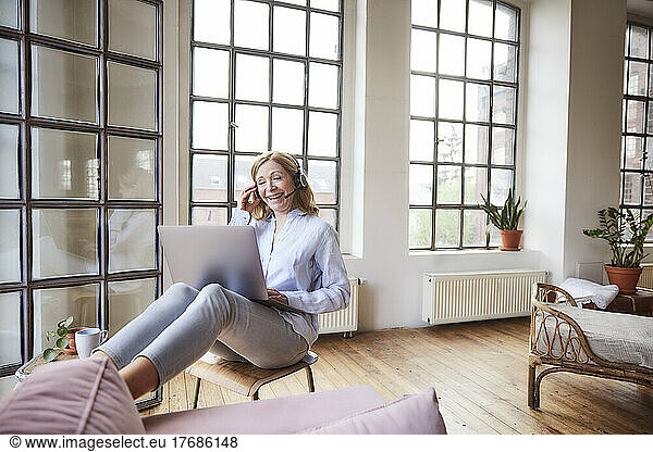 Smiling freelancer wearing headset talking on video call through laptop at home