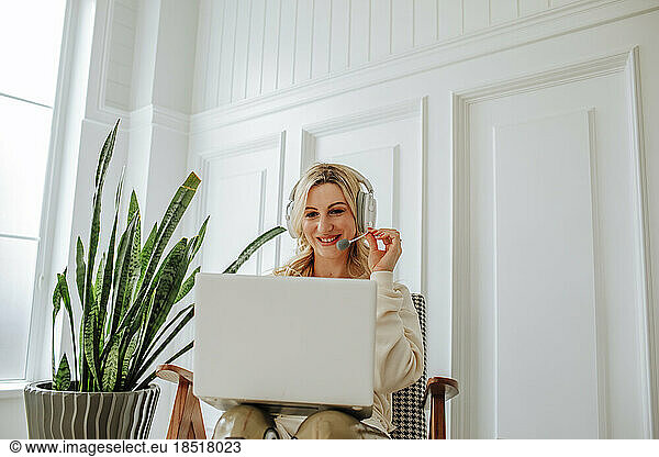 Smiling freelancer wearing headset using laptop at home