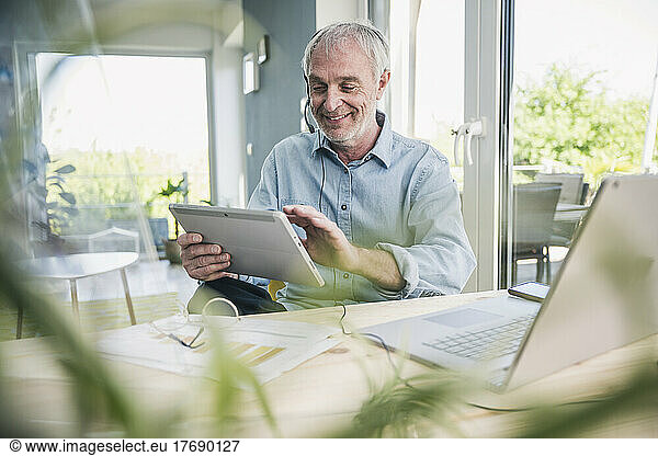 Smiling freelancer wearing headset using tablet PC at home