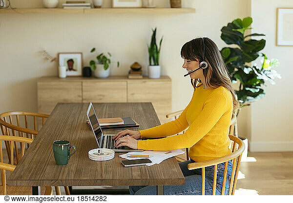 Smiling freelancer wearing headset working on laptop at home office