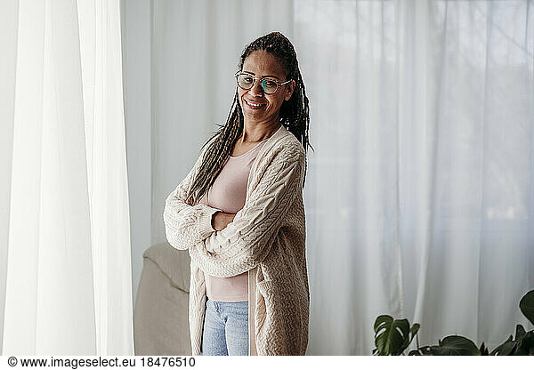 Smiling freelancer with arms crossed standing in front of curtains