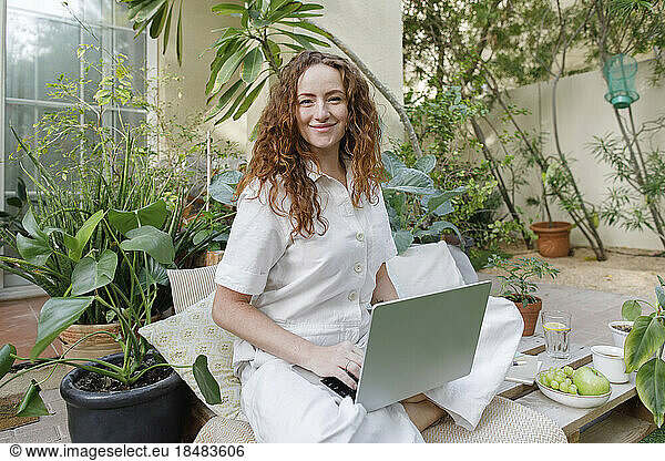 Smiling freelancer with cross-legged using laptop at backyard