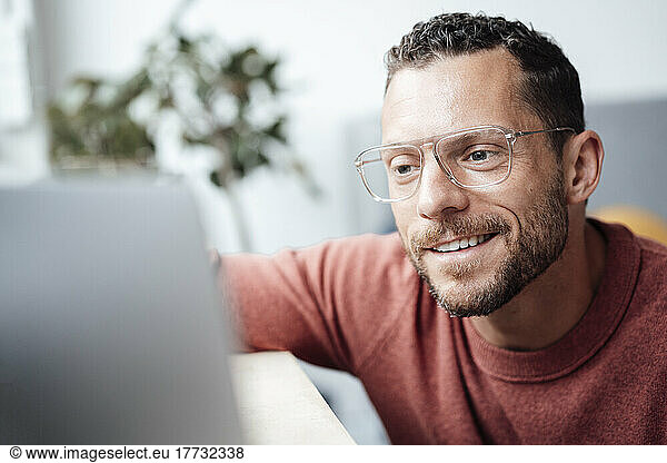 Smiling freelancer with eyeglasses looking at laptop