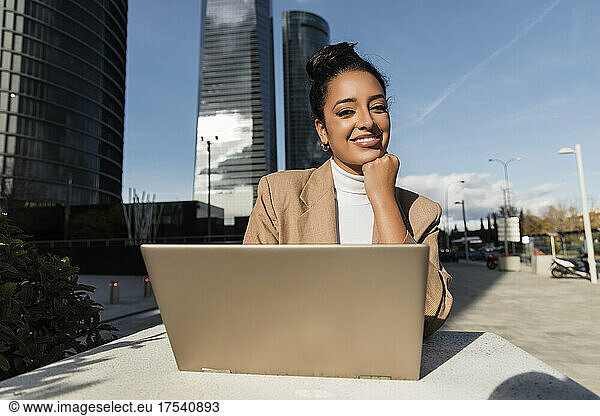 Smiling freelancer with laptop sitting at table on sunny day