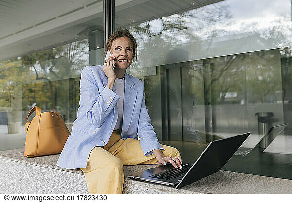 Smiling freelancer with laptop talking on phone