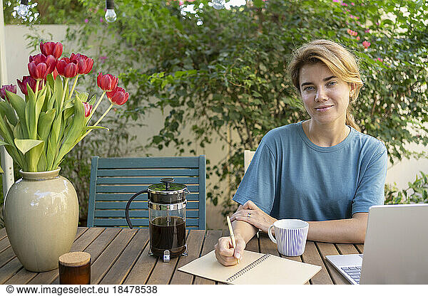 Smiling freelancer with pen and diary sitting at table in garden