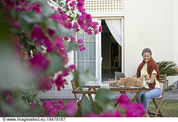 Smiling freelancer with pet cat sitting on chair in back yard