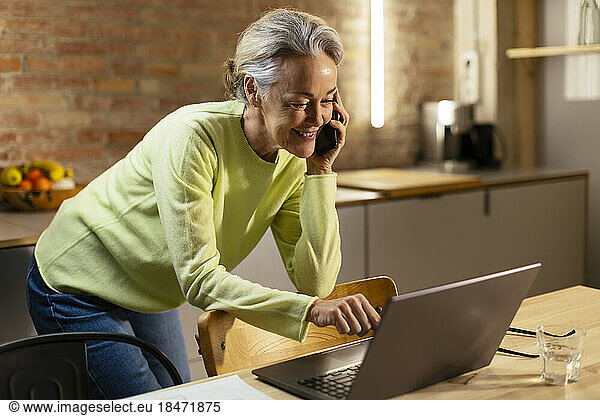 Smiling freelancer working over laptop and talking on mobile phone