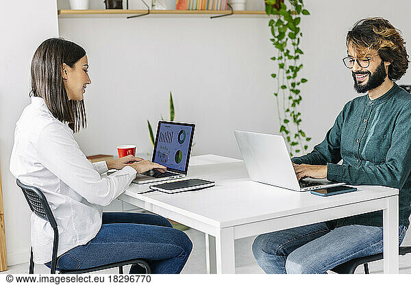 Smiling freelancers using laptops at desk in office
