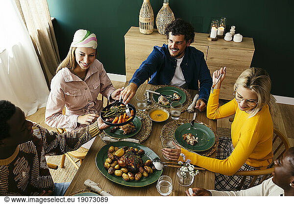 Smiling friends enjoying lunch at dining table in home