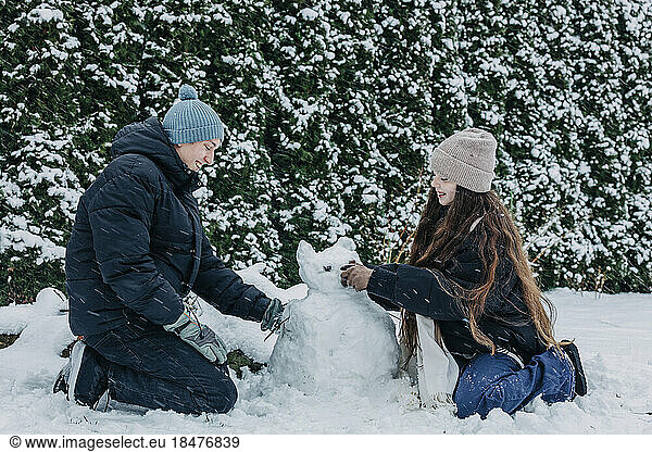 Smiling friends making snowman in winter at park