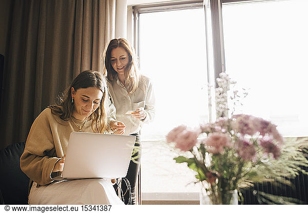 Smiling friends shopping online with credit card through laptop in hotel room
