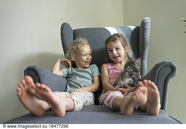 Smiling friends sitting together in armchair at home
