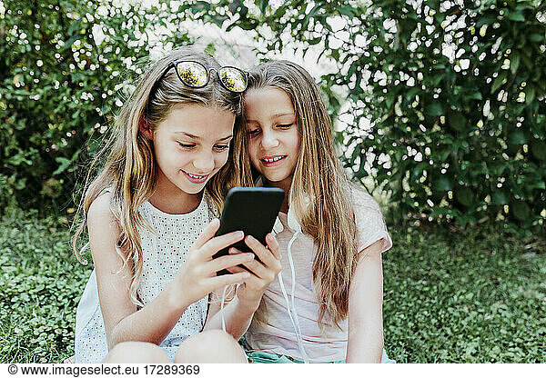 Smiling friends using mobile phone in garden