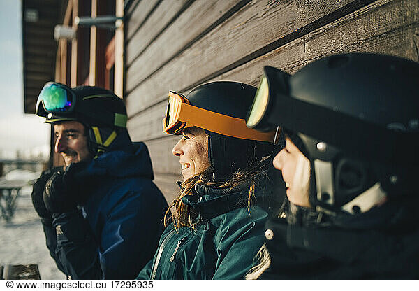 Smiling friends wearing sports helmets at ski resort during sunset