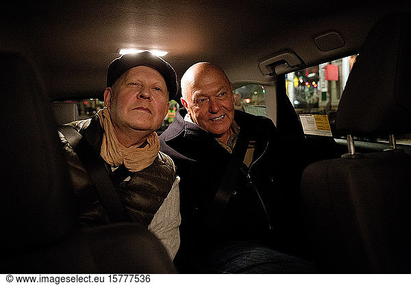 Smiling gay couple sitting in car at night