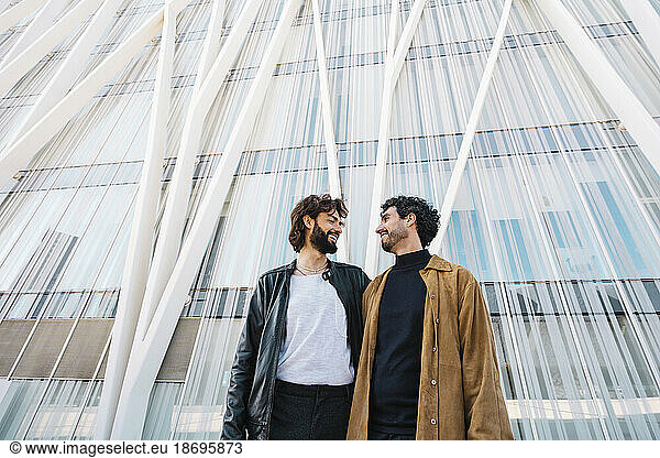 Smiling gay couple standing in front of building
