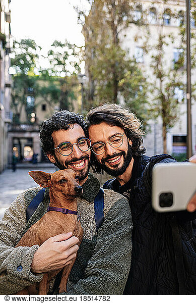 Smiling gay couple taking selfie with dog