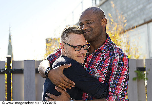 Smiling gay men embracing against fence