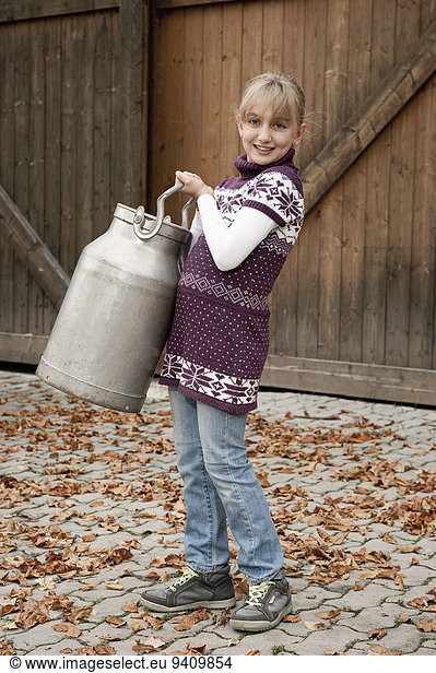 Smiling girl carrying milk churn on farm