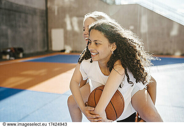 Smiling girl carrying piggyback to female friend at sports court