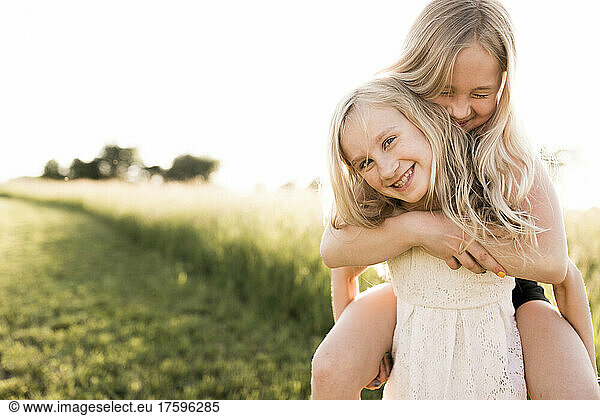 Smiling girl carrying sister piggyback at agricultural field