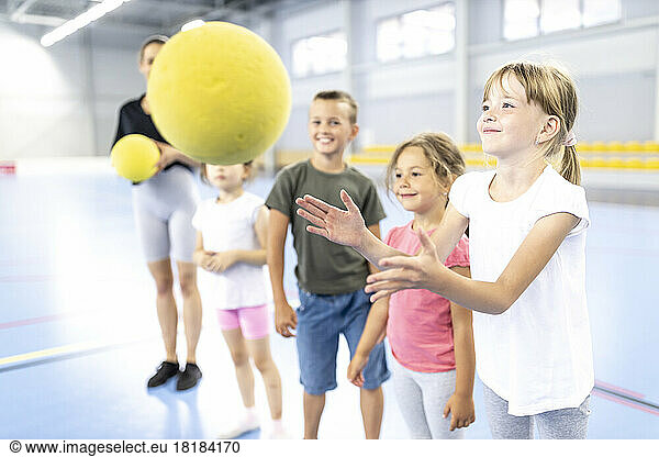 Smiling girl catching ball with friends at school sports court