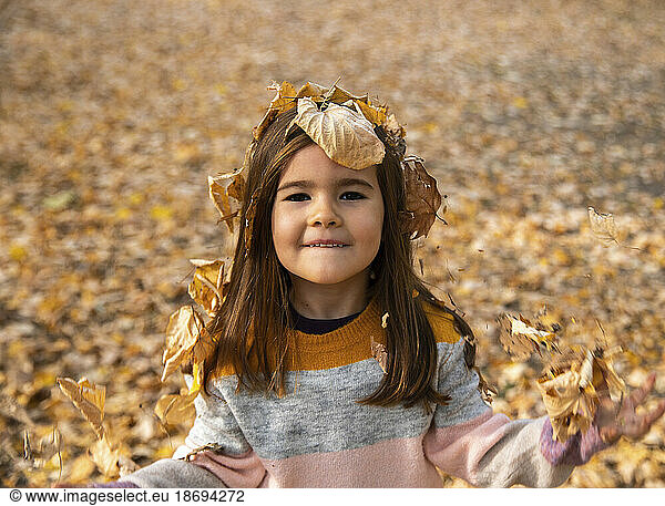 Smiling girl covered in dry leaves at autumn park