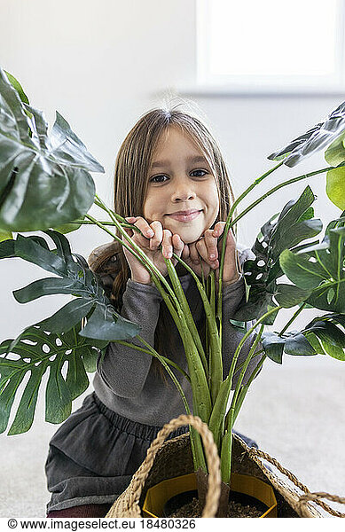 Smiling girl crouching by plant at home
